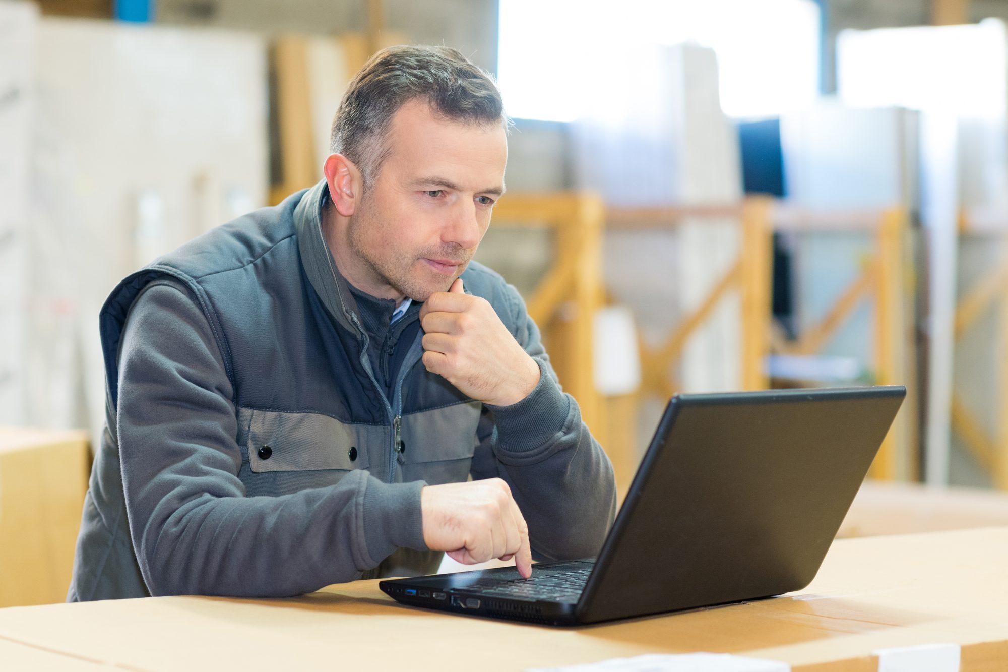 A building operations manager reviewing a system on a laptop in a warehouse