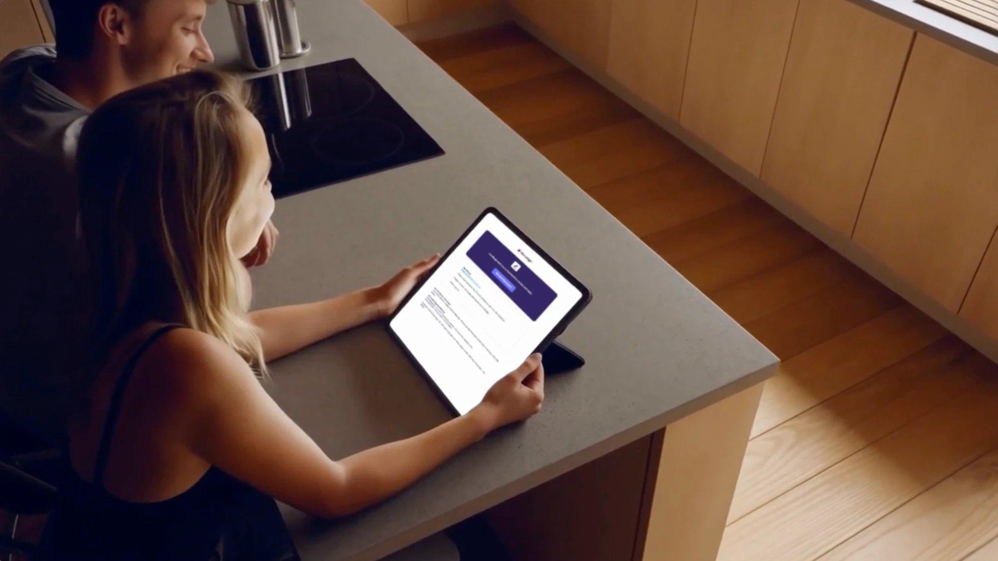 A couple at a kitchen bench reviewing a DocuSign document on a tablet, ready to sign