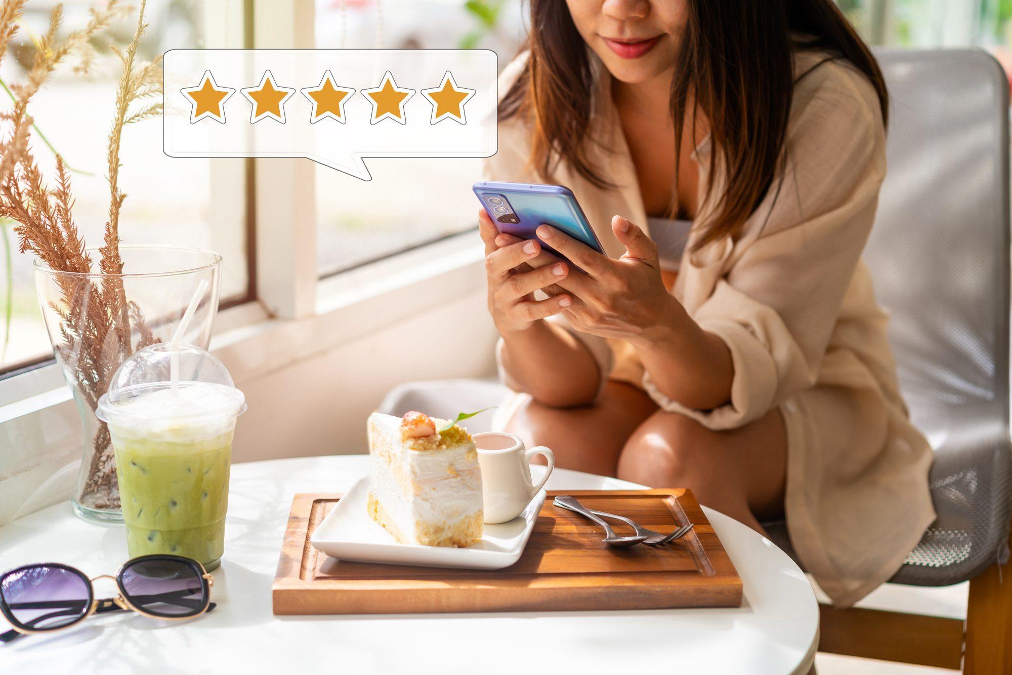 A woman in a café using her phone, with a five-star rating shown in a speech bubble above her
